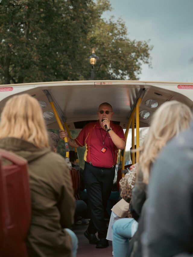Tour guide engaging visitors on an open-top bus tour in London, UK.
